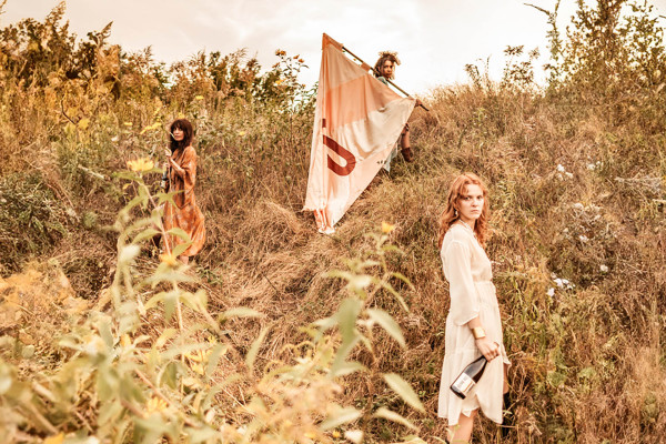 drei junge Frauen mit Fahne in einer Landschaft mit Weinflasche