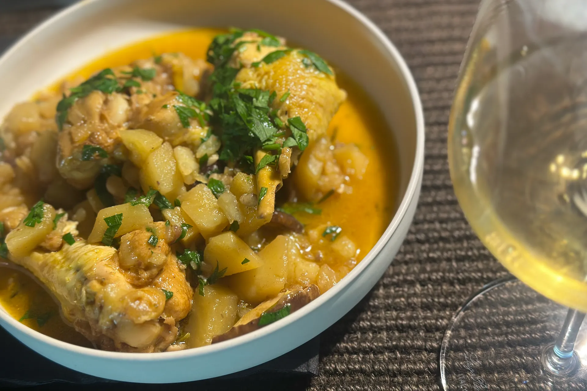 ein Teller mit einem Hühncheneintopf und einem Glas Wein daneben