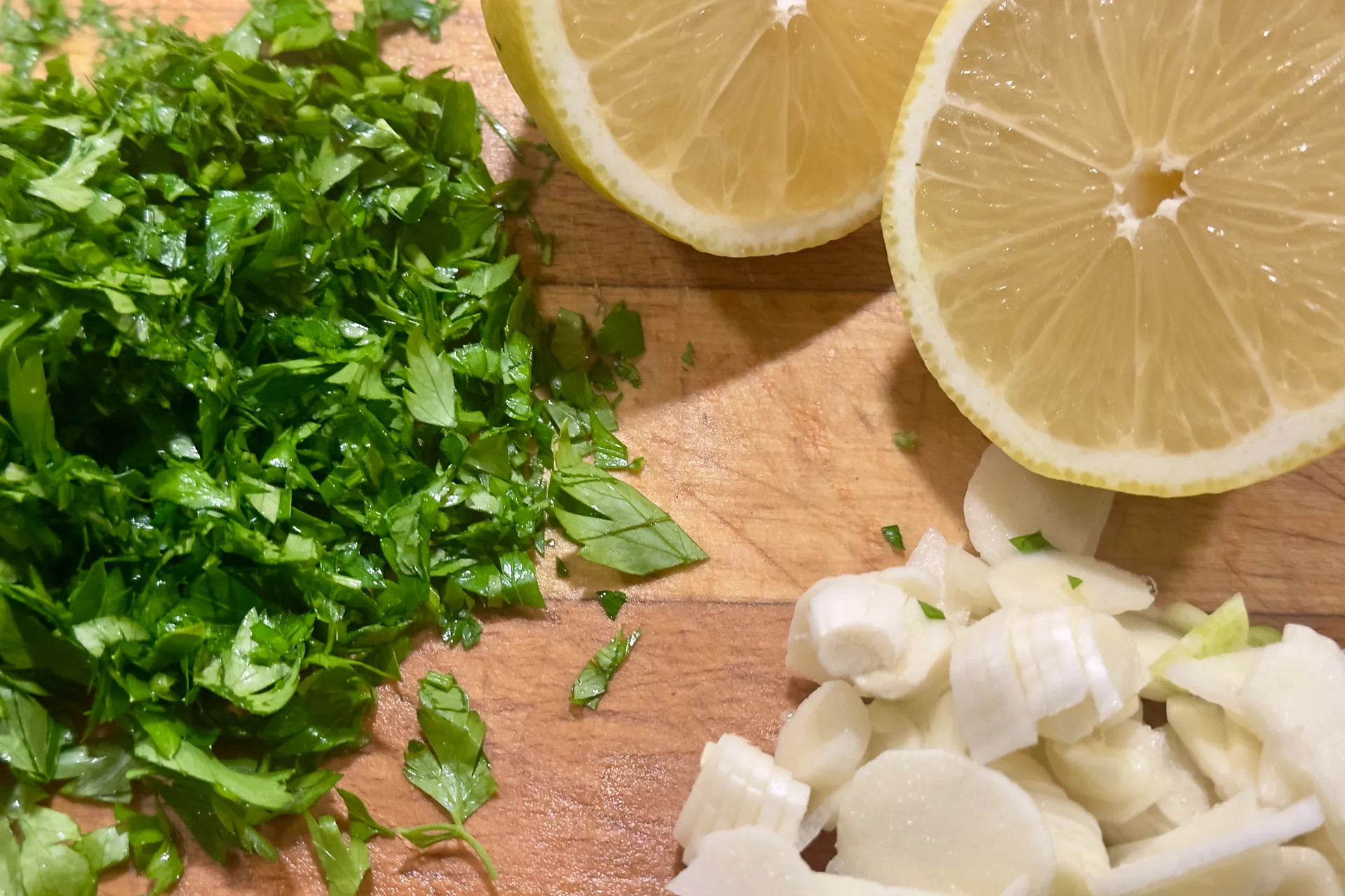 Petersilie Zitrone und Knoblauch liegt geschnitten und vorbereitet auf auf einem Holzbrett