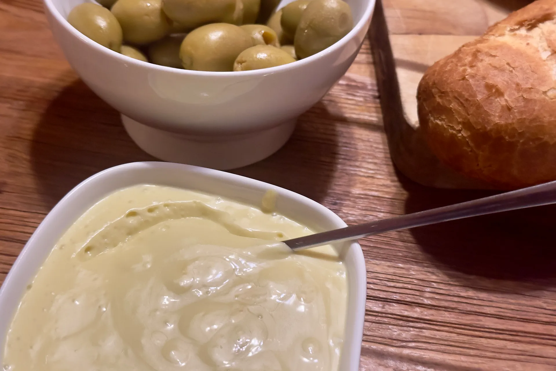 Ein Holztisch mit einer Schale Oliven mit Brot und einem Schälchen mit Aioli