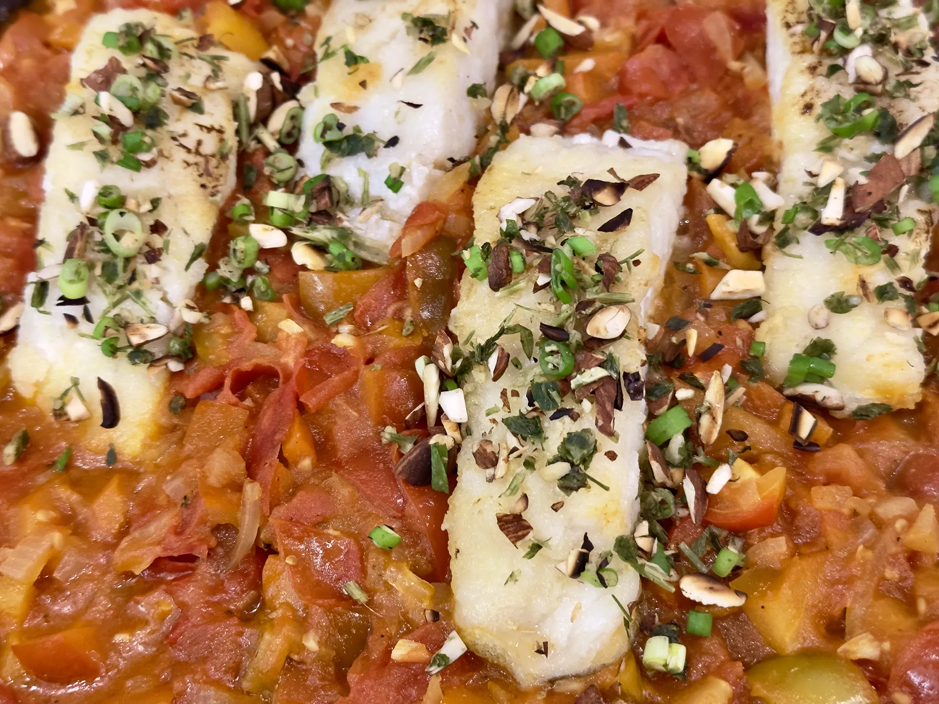 Fischfilets in einer Pfanne mit Tomatensauce und Kräuter Mandel Topping