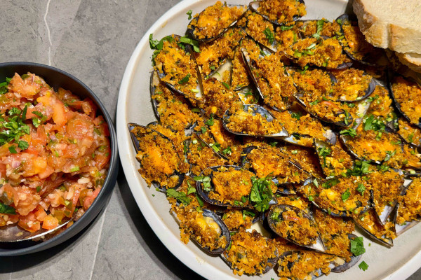 Überbackene Miesmuscheln auf weißer Platte mit gehackter Tomaten-Kräuter-Salsa und Weißbrot