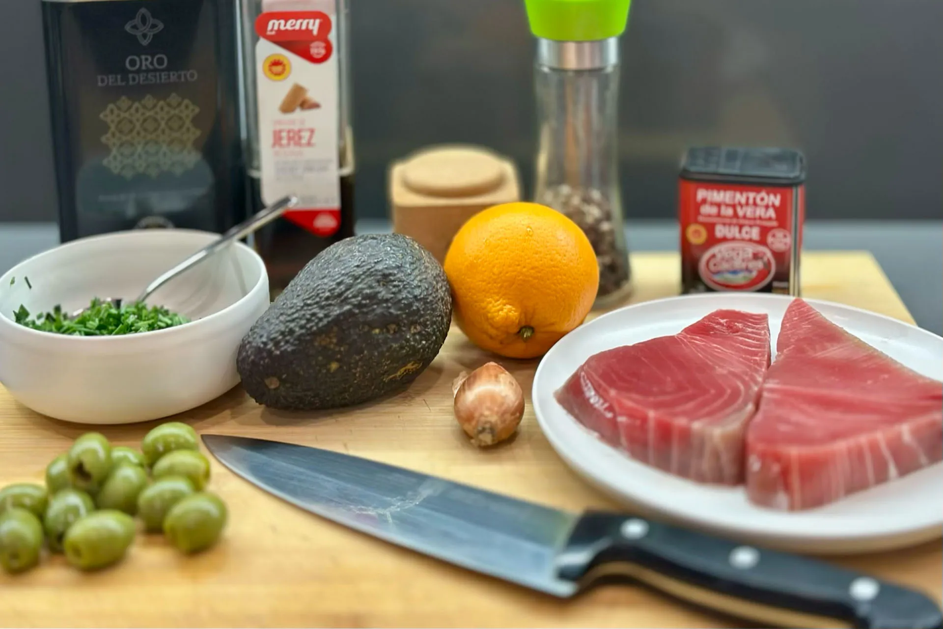 Zutaten für Thunfischtartar: frischer Thunfisch, Avocado, Orange, grüne Manzanilla-Oliven, Pimentón de la Vera, Schalotte, Sherry-Essig und Olivenöl auf Holzbrett
