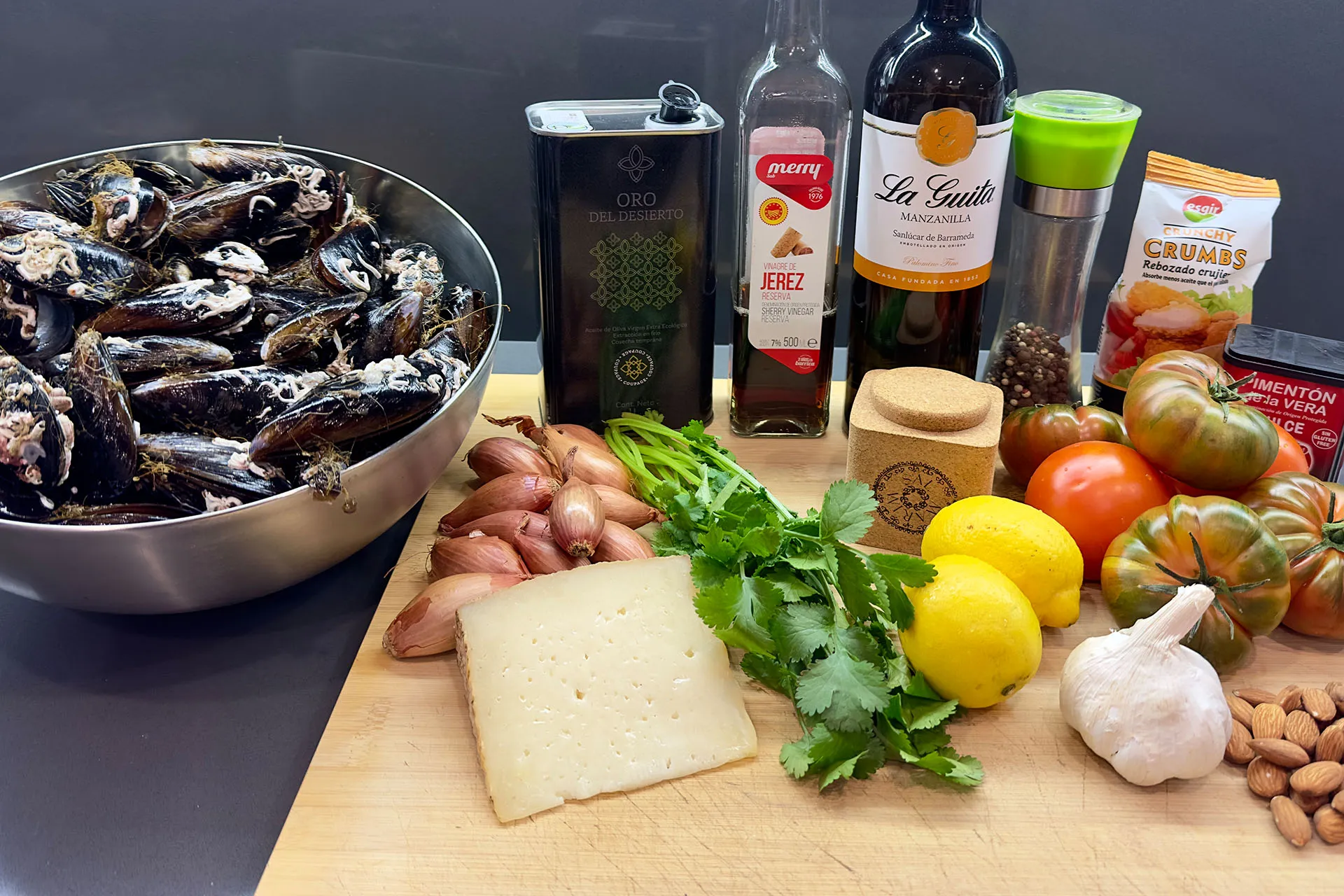 Zutaten für überbackene Miesmuscheln: frische Muscheln, Manzanilla, Olivenöl, Tomaten, Käse, Schalotten, Zitronen, Knoblauch und Mandeln auf Holzbrett